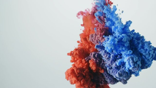 Red and blue colored liquids exploding and mixing in slow motion.