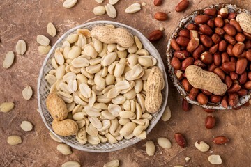 Peanuts peeled and in shell, in ceramic plate, brown background, top view.