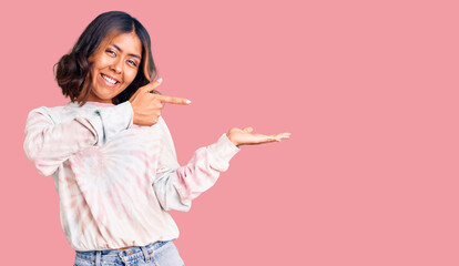 Young beautiful mixed race woman wearing casual tie dye sweatshirt amazed and smiling to the camera while presenting with hand and pointing with finger.