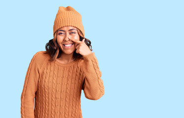 Young beautiful mixed race woman wearing wool sweater and winter hat pointing with hand finger to face and nose, smiling cheerful. beauty concept