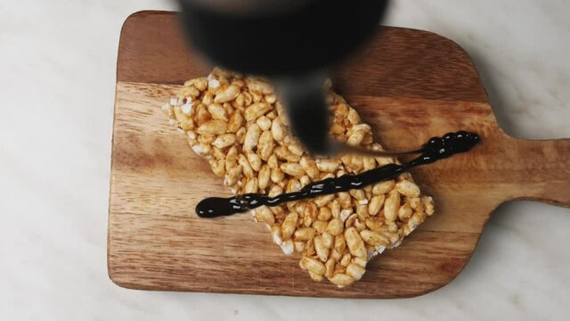 Pouring of chocolate on crispy rice bar, top view