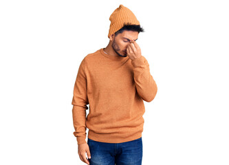 Handsome latin american young man wearing winter sweater and wool hat tired rubbing nose and eyes...