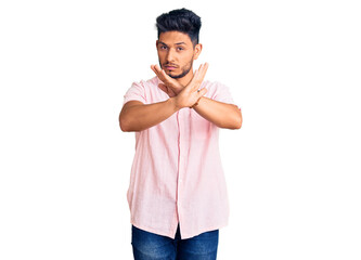 Handsome latin american young man wearing casual summer shirt rejection expression crossing arms doing negative sign, angry face