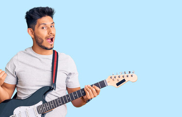 Obraz premium Handsome latin american young man playing electric guitar pointing thumb up to the side smiling happy with open mouth