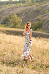 Beautiful red-haired girl is having fun and dancing in a field at sunset