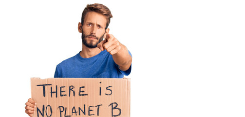 Handsome blond man with beard holding there is no planet b banner pointing with finger to the camera and to you, confident gesture looking serious