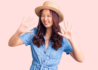 Obraz na płótnie Canvas Young beautiful chinese girl wearing summer hat showing and pointing up with fingers number ten while smiling confident and happy.