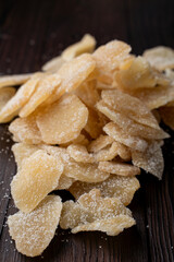 Heap of caramelized and dried ginger slices on dark wooden table, close up