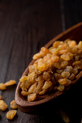 Close up of golden raisins in a wooden bowl, close up, dark background, studio photo with soft light