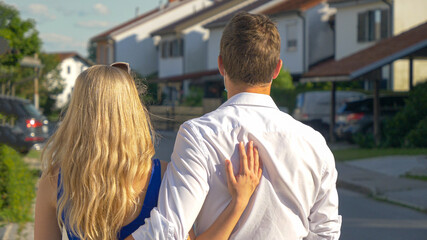 CLOSE UP: Unrecognizable millennial couple walks embraced down an empty street.