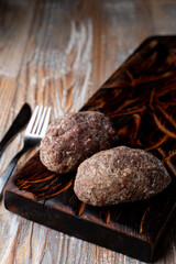 Semi prepared, ready to cook meat patties on a dark wooden cutting board, catalogue photo