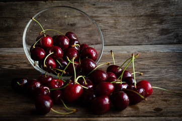 Ripe red cherries in glassware scattered on wooden boards.