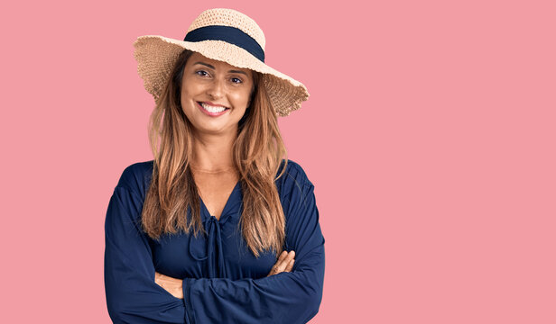 Middle age hispanic woman wearing summer hat happy face smiling with crossed arms looking at the camera. positive person.