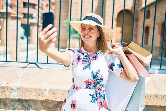 Middle age woman holding shopping bags making selfie by the smartphone at the city