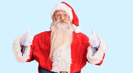 Old senior man with grey hair and long beard wearing traditional santa claus costume success sign doing positive gesture with hand, thumbs up smiling and happy. cheerful expression and winner gesture.