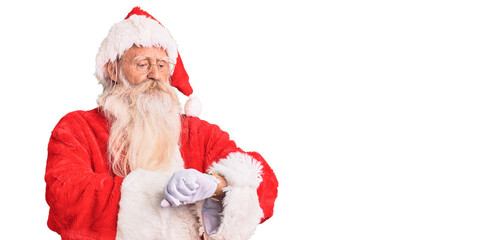 Old senior man with grey hair and long beard wearing traditional santa claus costume checking the time on wrist watch, relaxed and confident