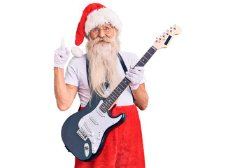 Old senior man with grey hair and long beard wearing santa claus costume playing electric guitar surprised with an idea or question pointing finger with happy face, number one