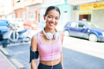 Young beautiful hispanic sport woman wearing runner outfit and headphones smiling happy at the town