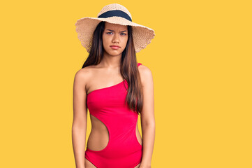 Young beautiful latin girl wearing swimwear and summer hat skeptic and nervous, frowning upset because of problem. negative person.