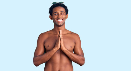 Fototapeta premium African handsome man wearing swimsuit and sunglasses praying with hands together asking for forgiveness smiling confident.