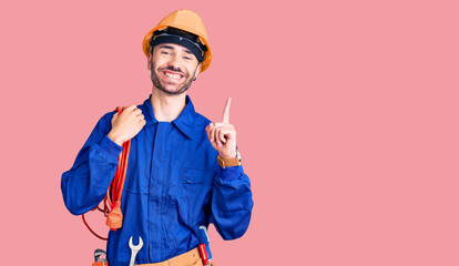 Young hispanic man wearing elecrician uniform holding cable surprised with an idea or question pointing finger with happy face, number one - obrazy, fototapety, plakaty
