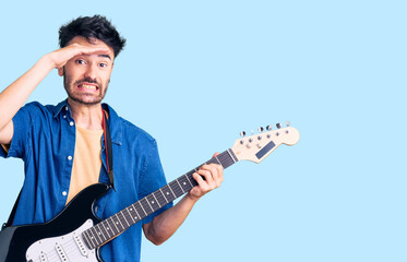 Obraz premium Young hispanic man playing electric guitar stressed and frustrated with hand on head, surprised and angry face