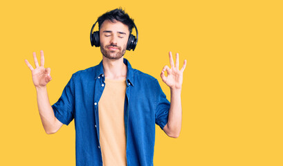 Young hispanic man listening to music using headphones relax and smiling with eyes closed doing meditation gesture with fingers. yoga concept.