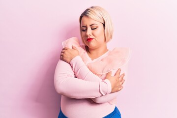 Young beautiful blonde plus size woman wearing casual sweater over isolated pink background hugging oneself happy and positive, smiling confident. Self love and self care