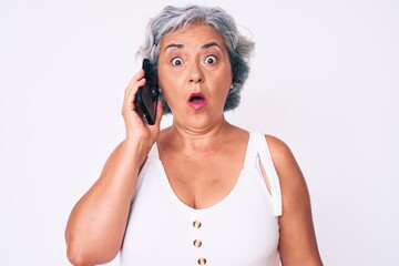 Naklejka premium Senior hispanic grey- haired woman having conversation talking on the smartphone scared and amazed with open mouth for surprise, disbelief face