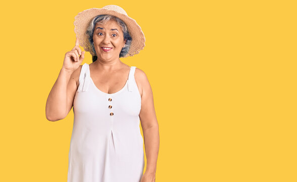 Senior woman with gray hair wearing summer hat and summer clothes pointing finger up with successful idea. exited and happy. number one.