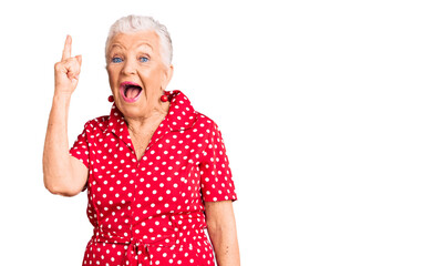 Senior beautiful woman with blue eyes and grey hair wearing a red summer dress pointing finger up...