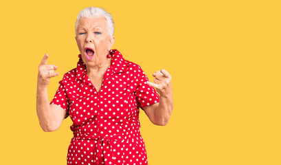Senior beautiful woman with blue eyes and grey hair wearing a red summer dress shouting with crazy...