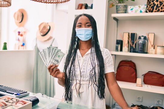 Young african american woman wearing medical mask holding dollars banknotes at clothing store