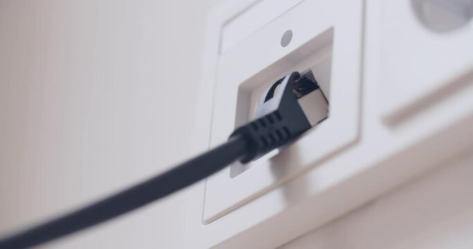 Hand plugging a computer network cable into a wall socket. Closeup shot.
