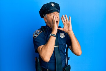 Handsome middle age mature man wearing police uniform shouting angry out loud with hands over mouth