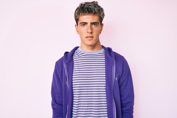 Young handsome man wearing casual purple sweatshirt with serious expression on face. simple and natural looking at the camera.