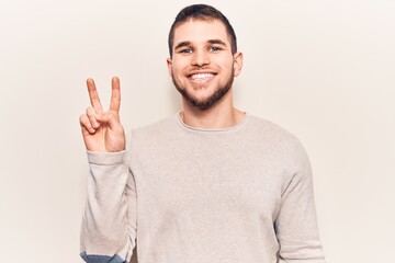 Naklejka premium Young handsome man wearing casual sweater smiling with happy face winking at the camera doing victory sign. number two.