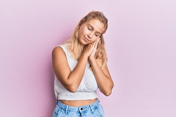 Young blonde girl wearing casual clothes sleeping tired dreaming and posing with hands together while smiling with closed eyes.