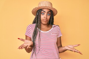 Young african american woman with braids wearing summer hat clueless and confused expression with...