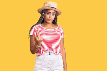 Young african american woman with braids wearing summer hat showing middle finger, impolite and rude fuck off expression