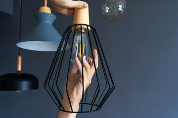 Close-up. A hand changes a light bulb in a stylish loft lamp. Spiral filament lamp. Modern interior decor.