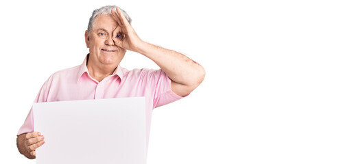 Senior grey-haired man holding blank empty banner smiling happy doing ok sign with hand on eye looking through fingers