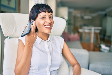 Beautiful brunette woman with short hair at home sitting on the sofa listening to voice message on the phone