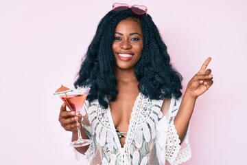 Beautiful african woman wearing summer look and drinking cocktail smiling happy pointing with hand and finger to the side