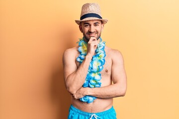 Young handsome bald man shirtless wearing swimwear and hawaiian lei smiling looking confident at...
