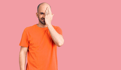 Young handsome man wering casual t shirt covering one eye with hand, confident smile on face and surprise emotion.