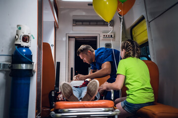 Naklejka premium Unconscious mother lying on a stretcher in an ambulance car, a paramedic providing her first aid.