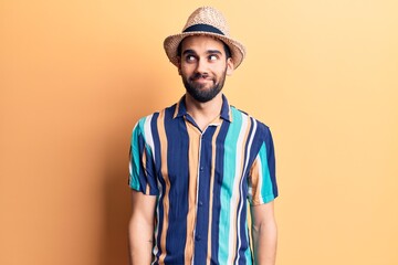 Young handsome man with beard wearing summer hat and shirt smiling looking to the side and staring away thinking.