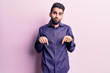 Young handsome man with beard wearing casual shirt pointing down looking sad and upset, indicating direction with fingers, unhappy and depressed.