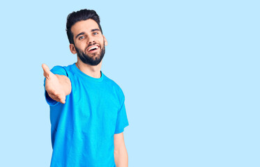 Young handsome man with beard wearing casual t-shirt smiling cheerful offering palm hand giving assistance and acceptance.